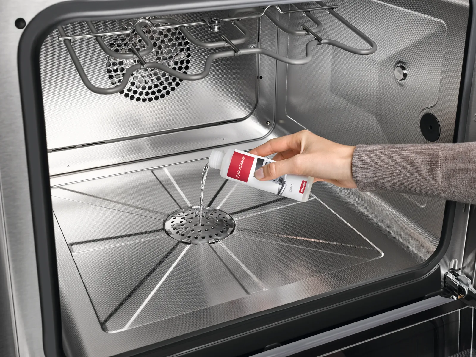 Hand gießt Miele HydroClean Reiniger in den Backofen